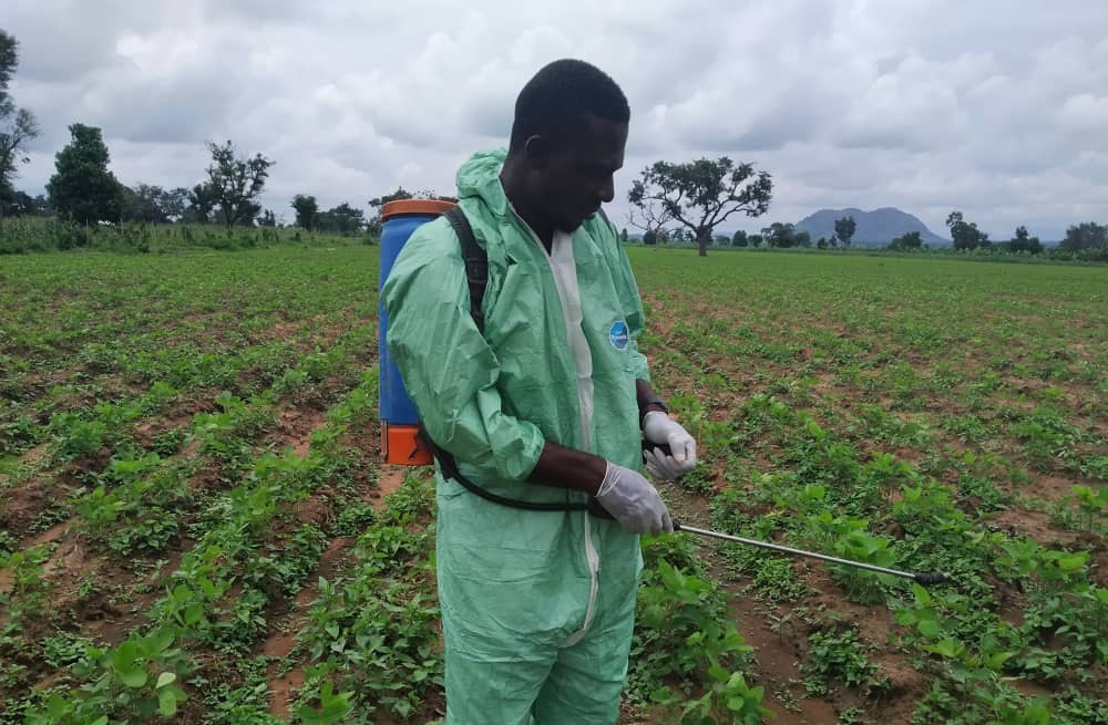 Emmy spraying young crops in a wide field under cloudy skies