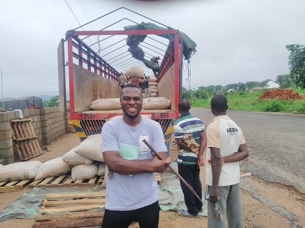 Emmy smiling in front of a truck being loaded with sacks of produce